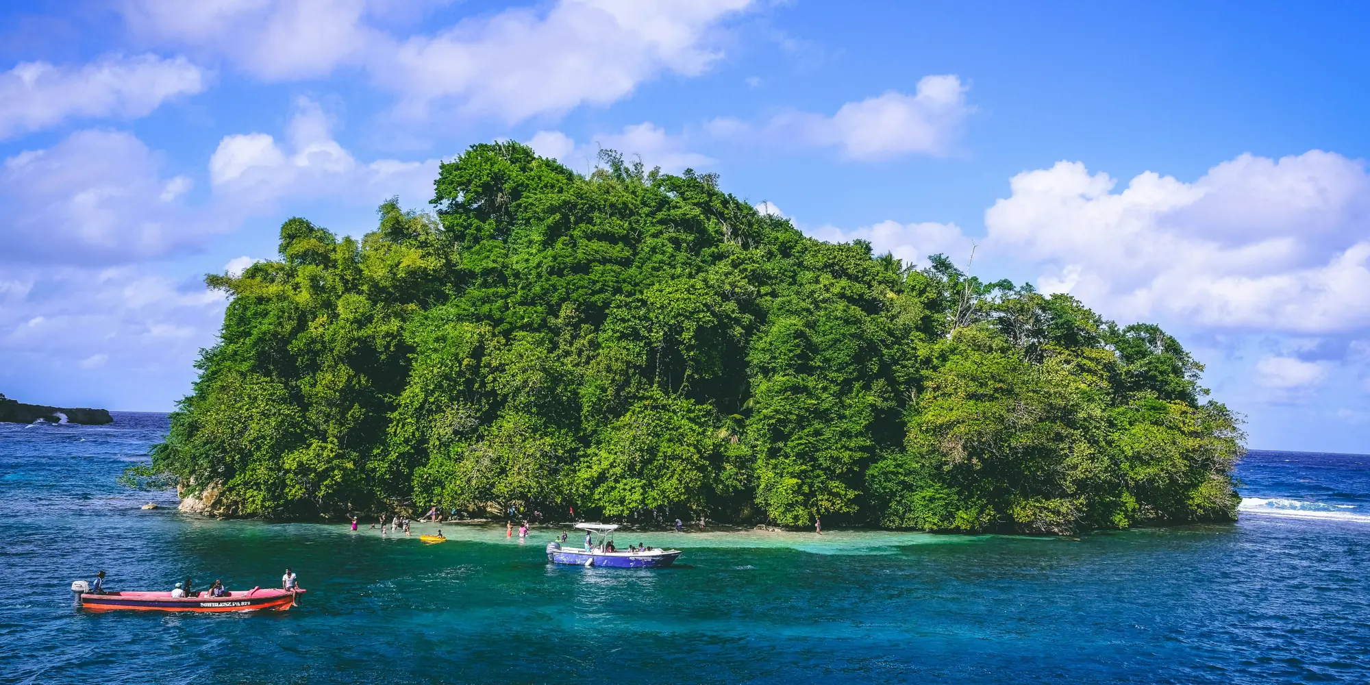 Small green island with boats in the sea off Jamaica diving with sharks