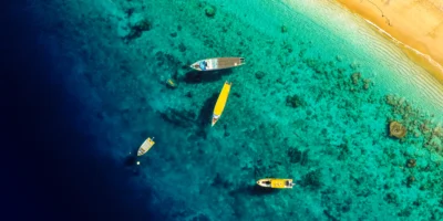 Luftaufnahme von Booten in türkisfarbenem Küstenwasser neben einem Sandstrand