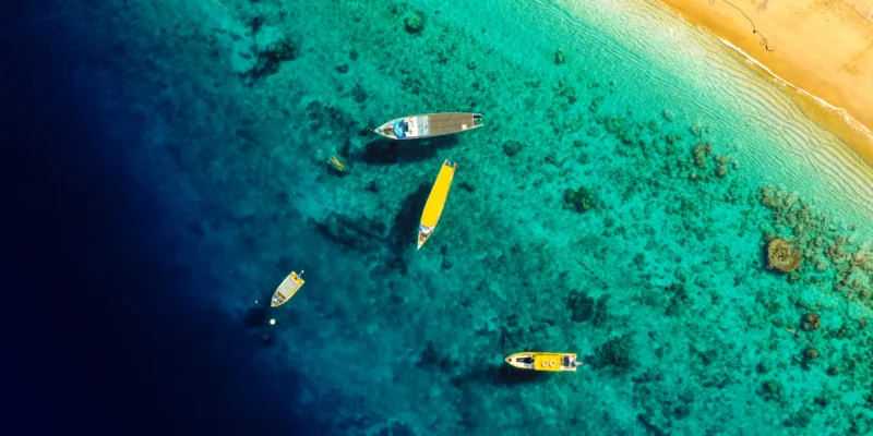 Luftaufnahme von Booten in türkisfarbenem Küstenwasser neben einem Sandstrand