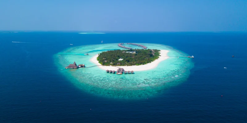Luftaufnahme einer bewaldeten Insel mit weißem Strand und türkisfarbener Lagune auf den Malediven