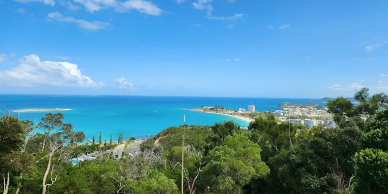 Blick von einem bewaldeten Hügel über die türkisfarbene Bucht und die Stadt Nouméa